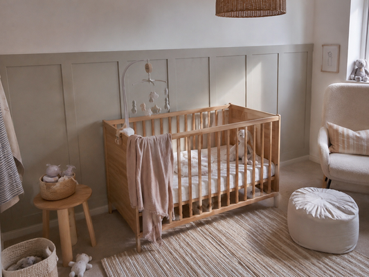 Neutral nursery with wood cot and panelled wall painted in a soft sage tone